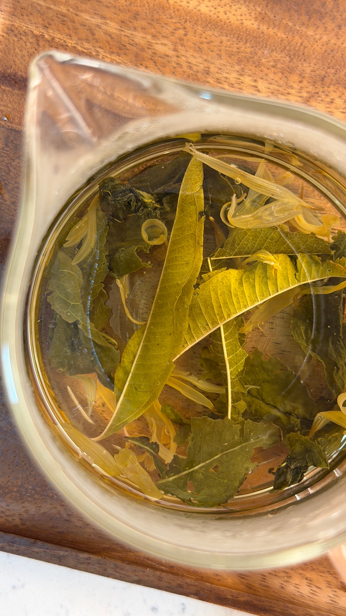 Fragrant Tie Guan Yin blended with Marigold and Lemon Verbena - showcasing its infusion in a beautiful glass beaker, best for viewing the leaves up close. 